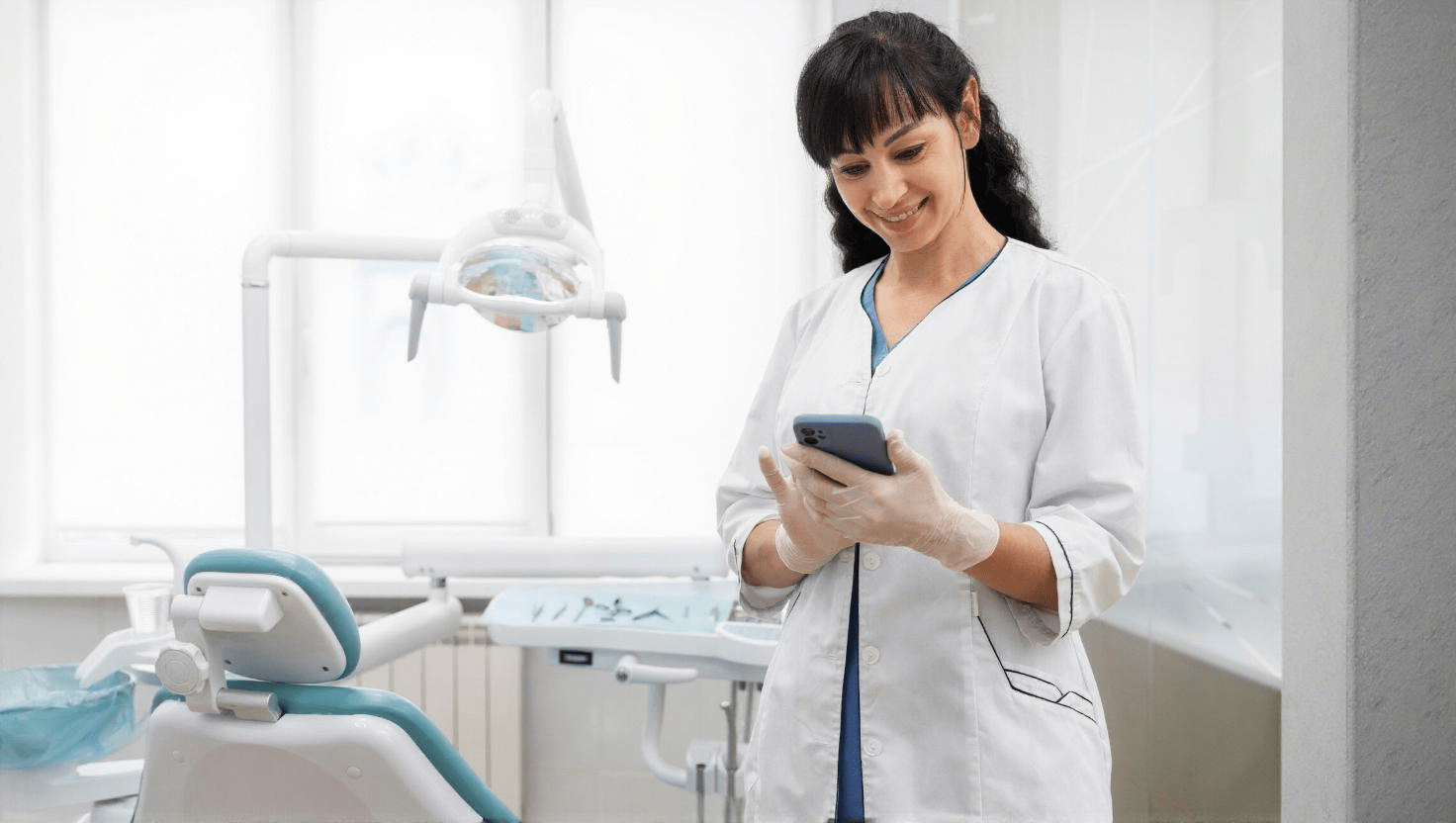 Phone Systems for Dental Offices: Enhancing Patient Communication in New England 1 Female dentist in exam room using mobile app feature of her tailored VoIP phone system for dental offices.
