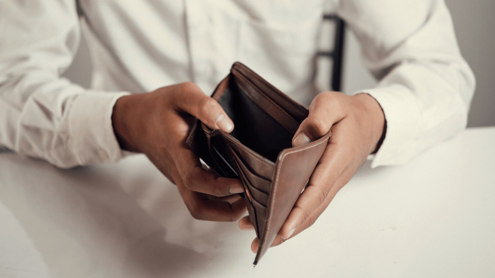 Grow Your Practice, Shrink Your Bill with Phone Services Built for New England Healthcare Providers 2 A man in a white shirt holds open an empty wallet while sitting at a table. This image highlights the financial strain faced by individuals and underscores the importance of affordable communication options provided by scalable phone systems and accessible phone services, especially for local businesses and customers.