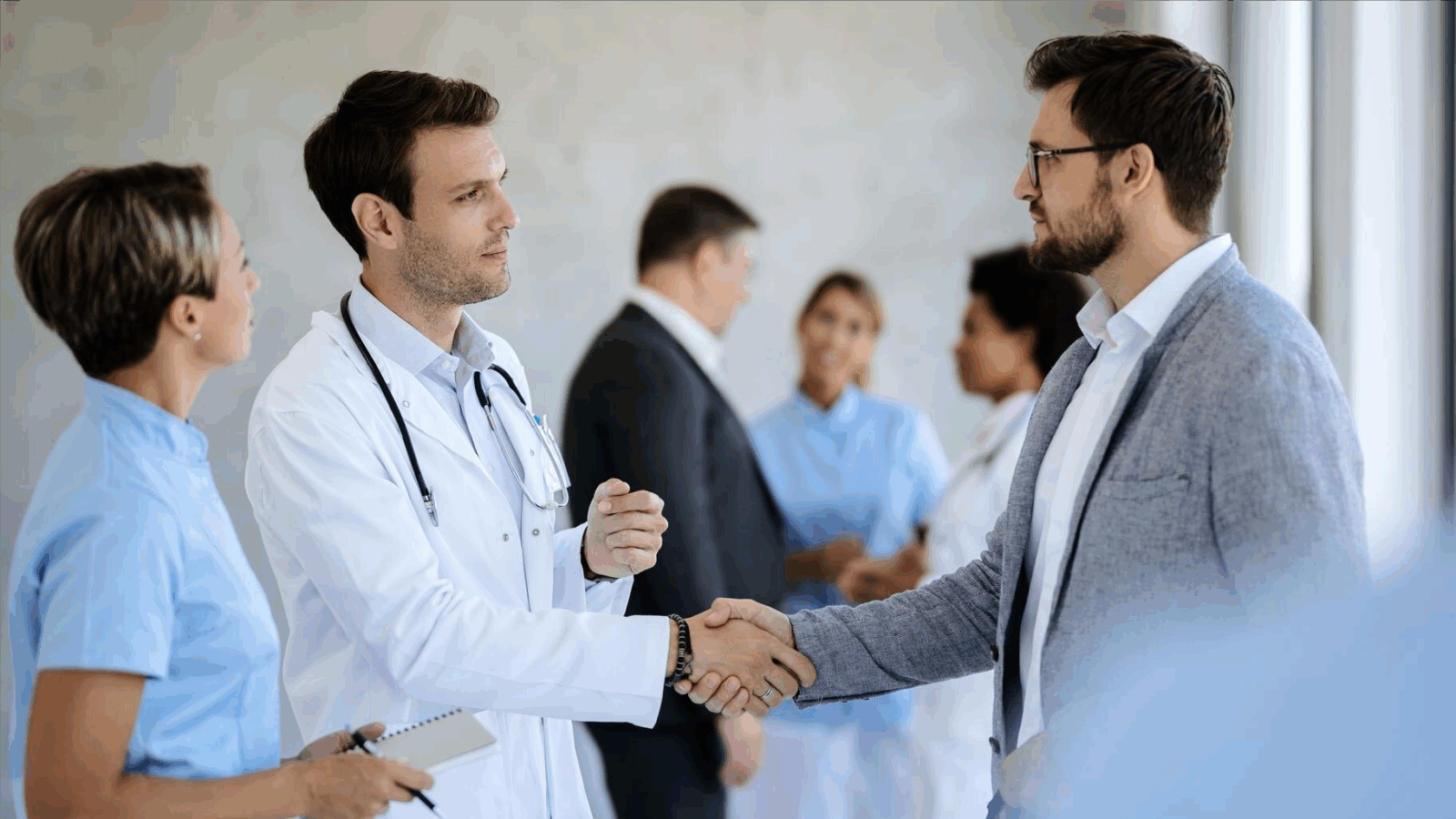 Grow Your Practice, Shrink Your Bill with Phone Services Built for New England Healthcare Providers 5 A doctor in a white coat shakes hands with a man in a blazer while colleagues converse in the background. This interaction reflects the trust and professionalism supported by local business telecom and scalable phone systems that ensure reliable and affordable communication in healthcare partnerships.
