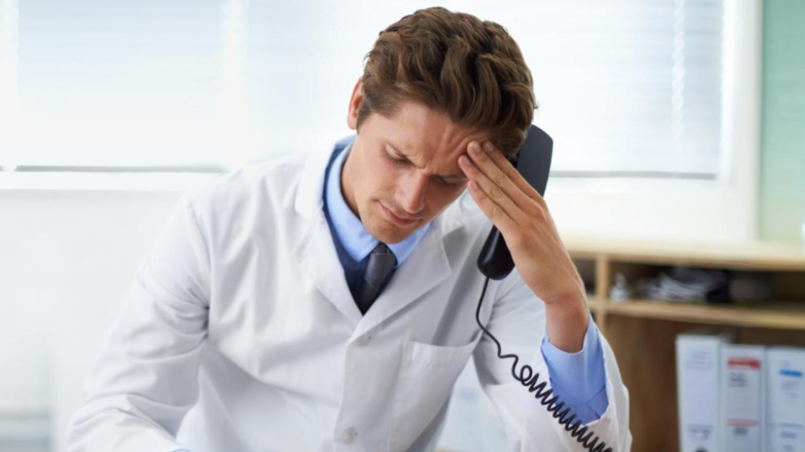 Survive the Summer Rush with the Right Phone Systems for Medical Offices in New England 2 Male doctor in a white coat looking stressed while on a call, highlighting strain on a medical office phone system.