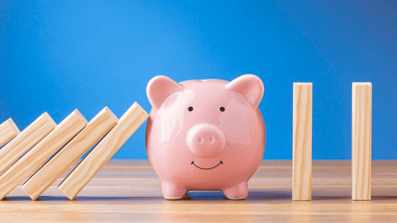 Avoid the Cost of Outages with 4G Backup Internet Connection 3 A pink piggy bank stopping a row of falling wooden dominoes on a table, symbolizing financial protection and stability through 4G Backup and wireless internet backup strategies.