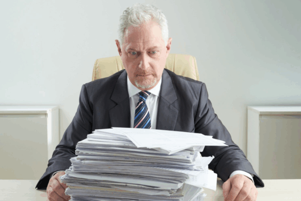 f6e0e098-4845-4721-8674-aa8d8d1e05ad A concerned businessman staring at a tall stack of bills, highlighting the financial risks of poor network redundancy and the need for reliable 4G Backup systems in business operations.