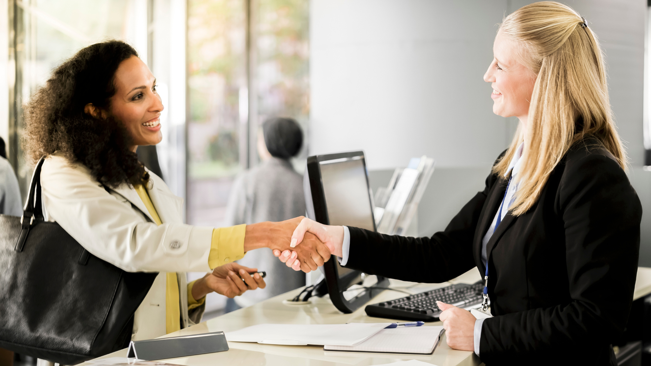 Two women smiling and shaking hands at a front desk, highlighting personalized customer experience that Rhode Island Telephone provides.