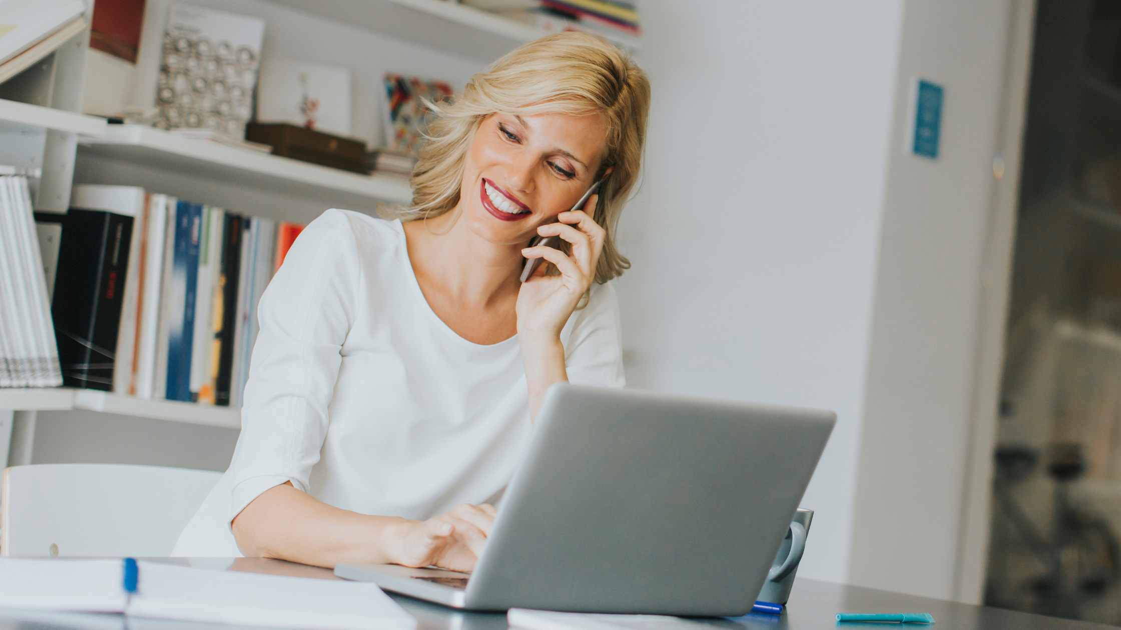 A remote employee smiling while on a phone call and using cloud-based collaboration tools for better business communications.