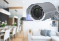 A close-up view of a security camera mounted indoors, with a blurred modern living room in the background. This image represents how surveillance solutions and advanced security systems can discreetly integrate into homes and businesses to enhance safety.