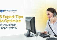 Smiling woman on a corded phone while typing at a desk, promoting tips to optimize your business phone system.