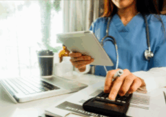 A nurse in scrubs uses a calculator while holding a tablet at a desk with a laptop and medical files. The scene represents the integration of phone services and local business telecom in healthcare settings, supporting affordable communication and scalable phone systems for efficient patient management.