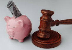 A close-up of a pink piggy bank with a rolled-up U.S. dollar bill inserted into the slot, placed next to a wooden judge’s gavel. This visual symbolizes financial decisions in the legal industry, representing how cost-saving telecom solutions like VoIP for law offices can reduce expenses and improve efficiency.